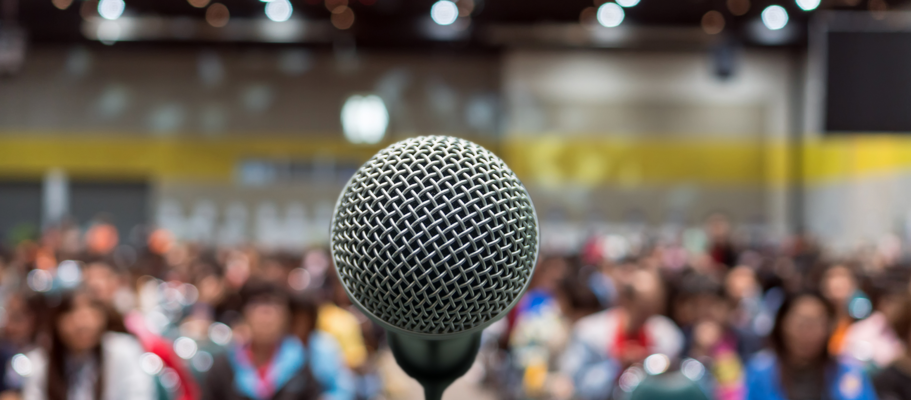 Close-up view of microphone, with an out of focus view of a crowd of seated people in the background